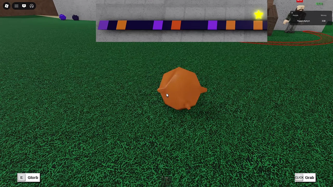 A round orange blob on grass, with a striped purple and orange colour bar above it